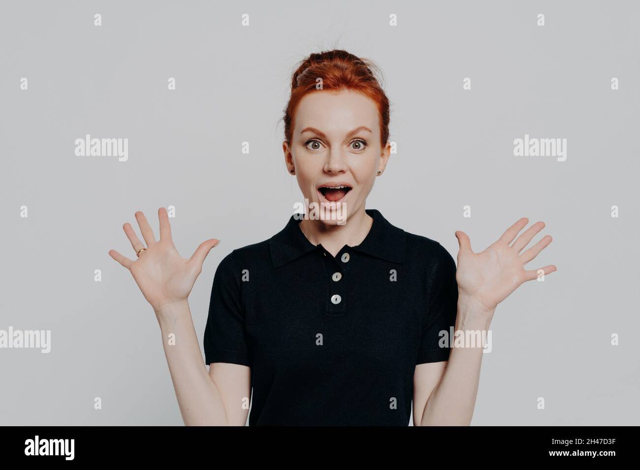 Young surprised emotional ginger girl raising hands and opening mouth with shocked face expression Stock Photo