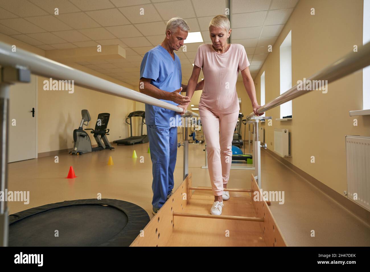 Female patient walking between parallel bars at rehabilitation room