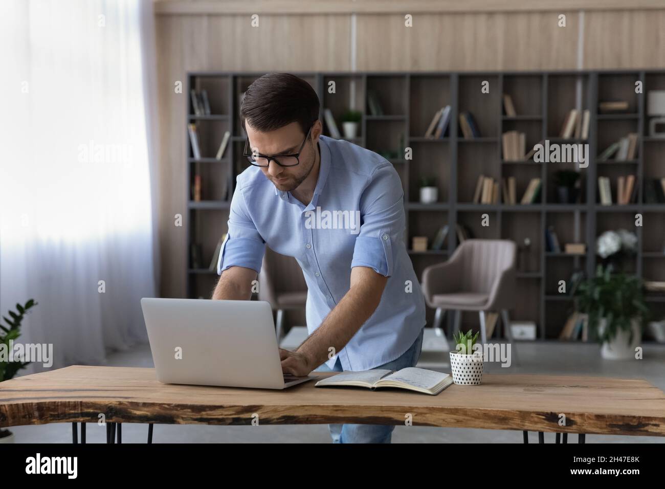 Concentrated young businessman working on computer, standing at table. Stock Photo
