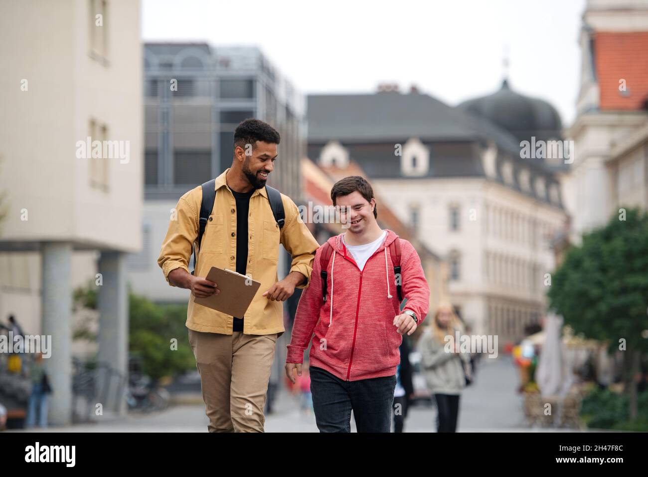 Young man with Down syndrome and his mentoring friend walking and talking outdoors Stock Photo