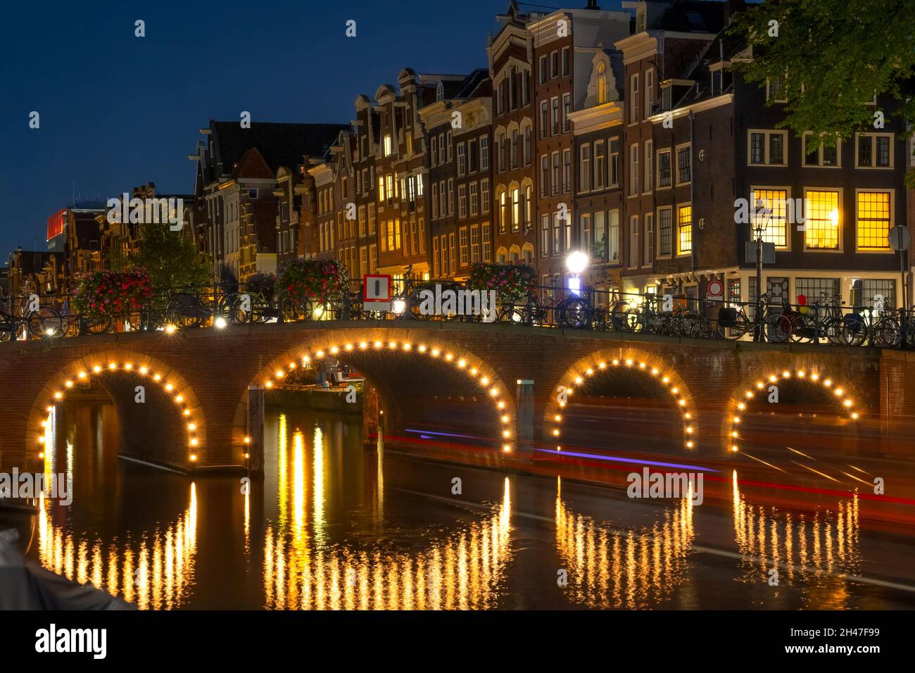 Netherlands. Night on the Amsterdam Canal. Illuminated bridge and boat trail. Traditional Dutch houses on the waterfront Stock Photo