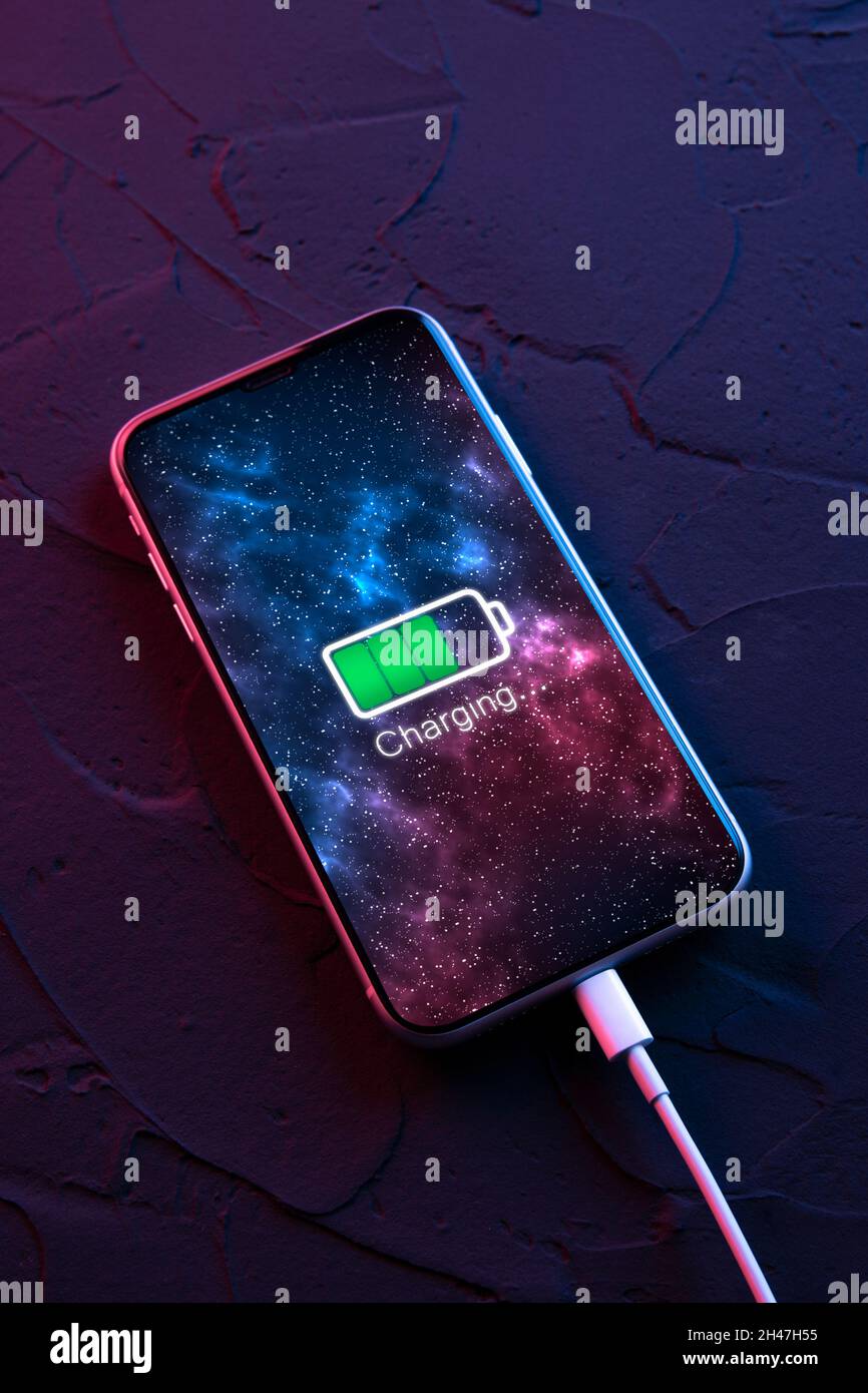 Mobile smart phone on wireless charging device on dark neon red and ...