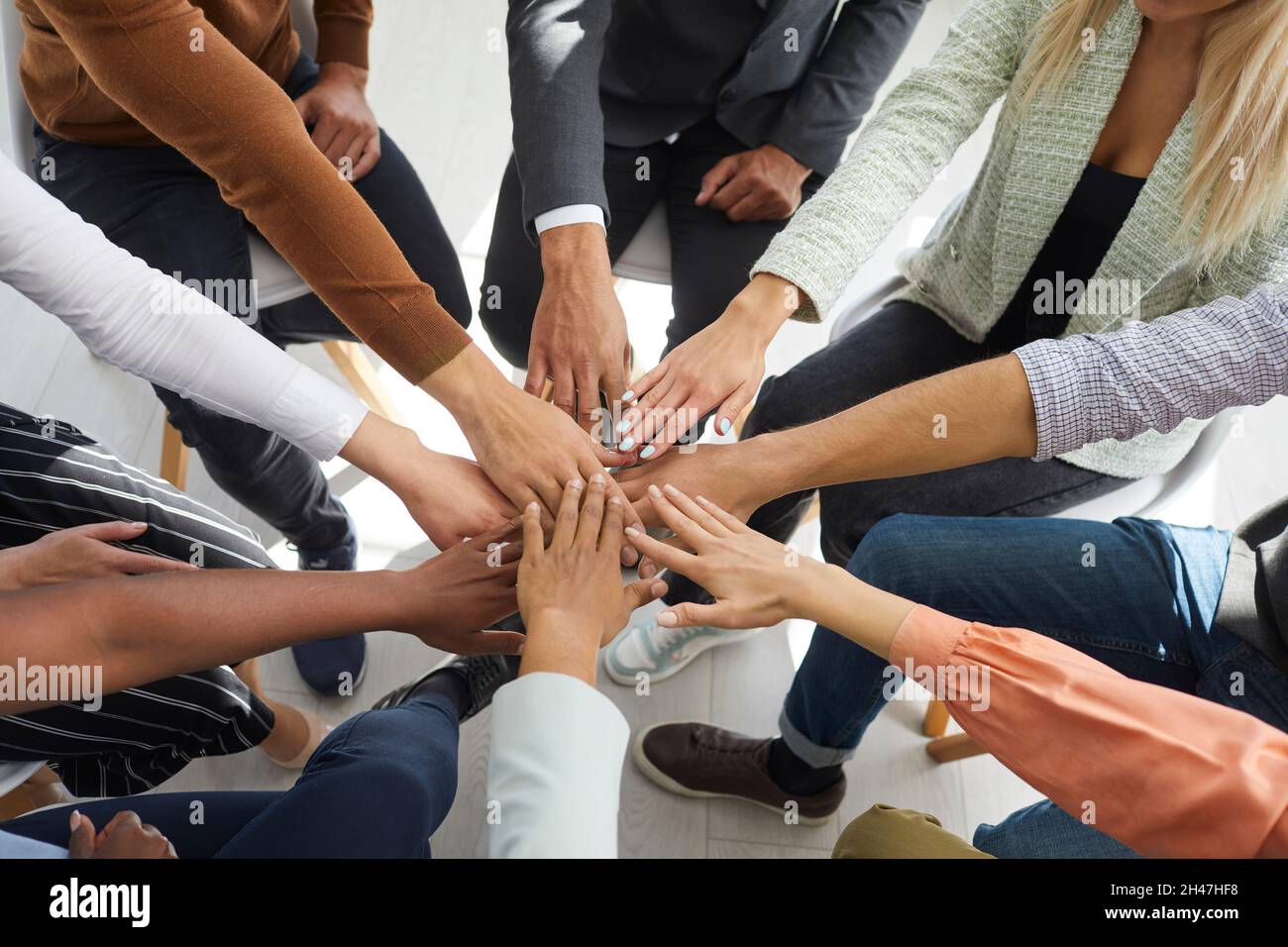 Young motivated people fold their hands on each other symbolizing their unity and support. Stock Photo