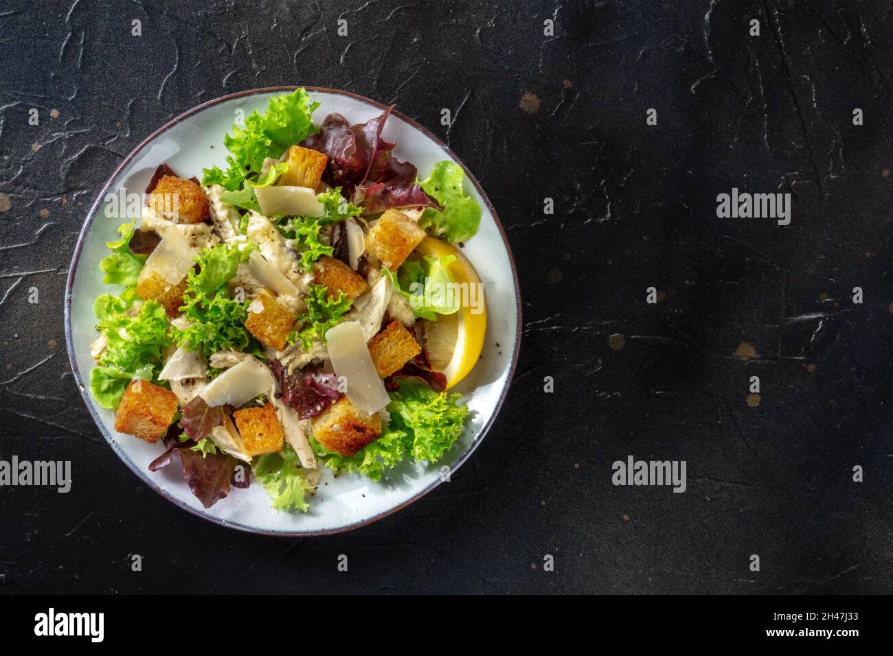 Chicken Caesar salad, overhead shot on a black background with a place for text Stock Photo