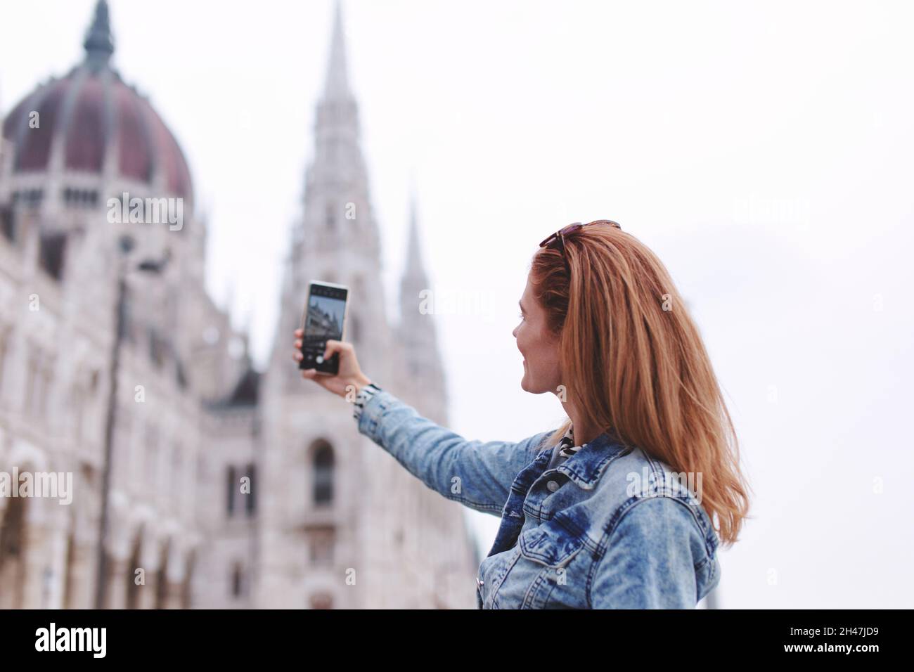 Young redhead woman taking photo of Hungarian Parliament building at Budapest, Hungary Stock Photo