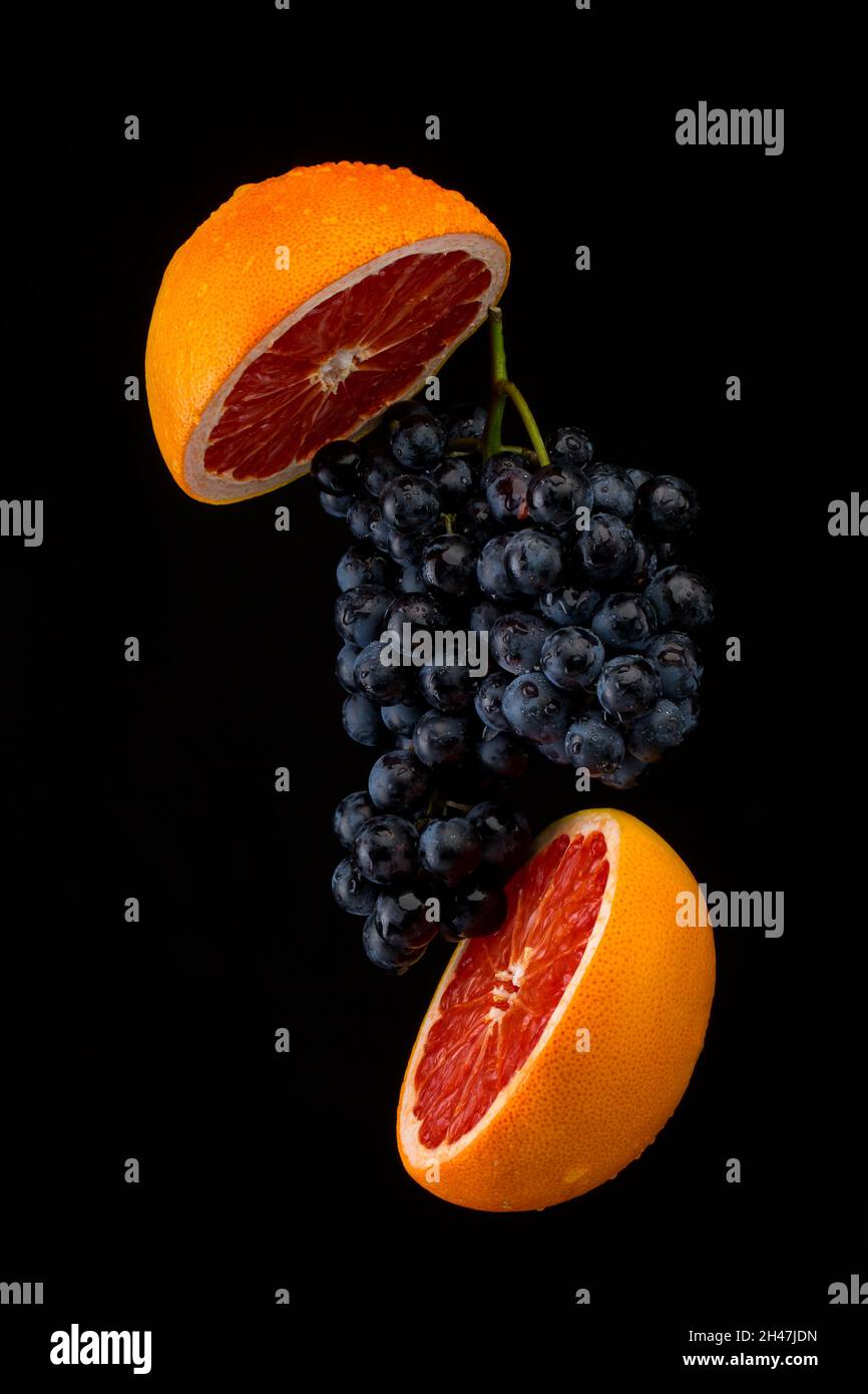 Dark blue grape with red grapefruit on black background Stock Photo