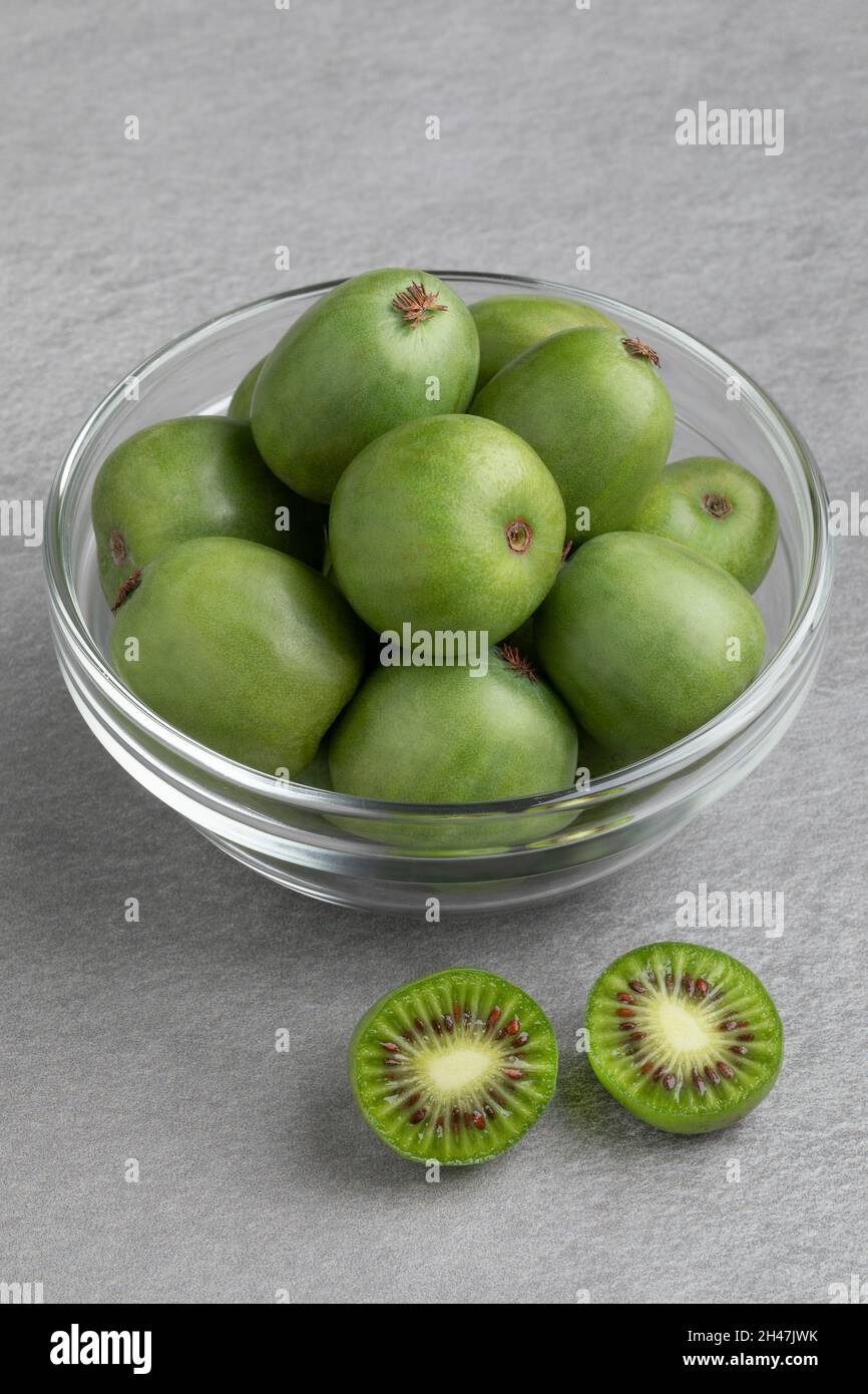 Glass bowl with fresh whole and halved kiwi berries close up Stock Photo