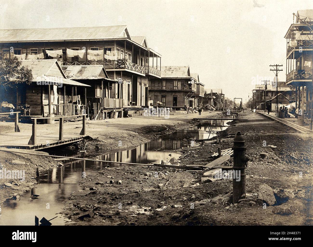 Colón, Panama, before the sanitary works that were implemented during the construction of the Panama Canal: a ditch runs down the centre of a street lined with wooden houses. Photograph, 1908. Stock Photo