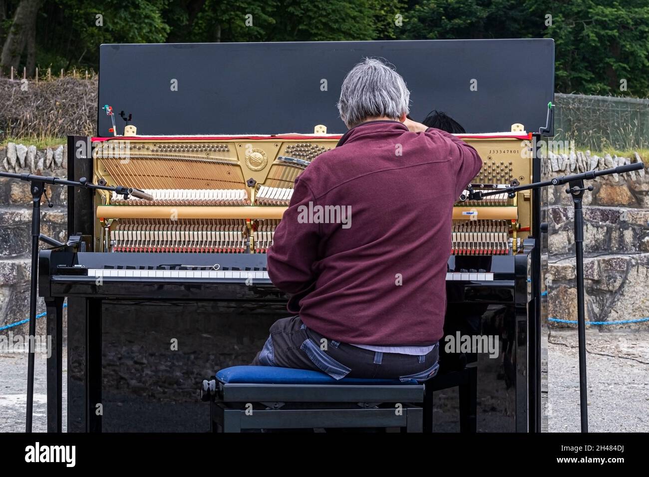 A piano tuner tuning an upright piano in preparation for an outdoor piano recital. Stock Photo