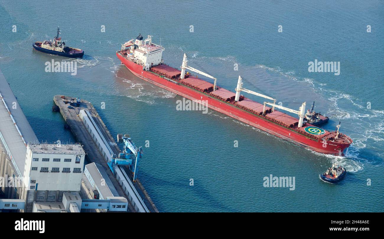 Ship between two tug boats being guided into Seaforth Docks, Liverpool, Merseyside, North West England, UK Stock Photo