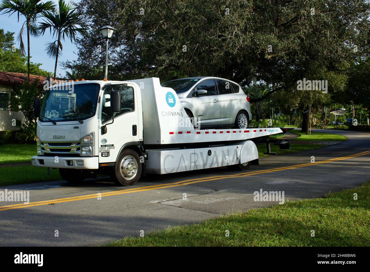 Carvana rollback delivery truck with Ford C-Max gas-electric hybrid in residential neighborhood Stock Photo