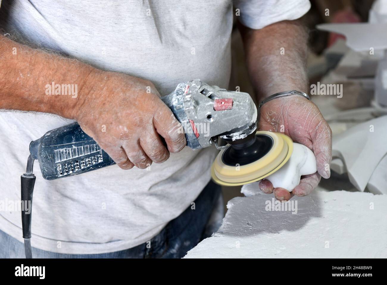 From above of crop unrecognizable male master using electric polisher while creating new marble souvenir in traditional workshop Stock Photo