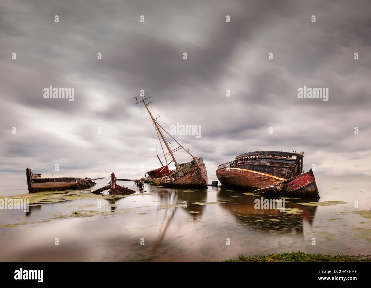 Wrecked boats and barges lying abandoned and partially submerged along the coast at Pin Mill on the river Orwell, Suffolk, England. Stock Photo
