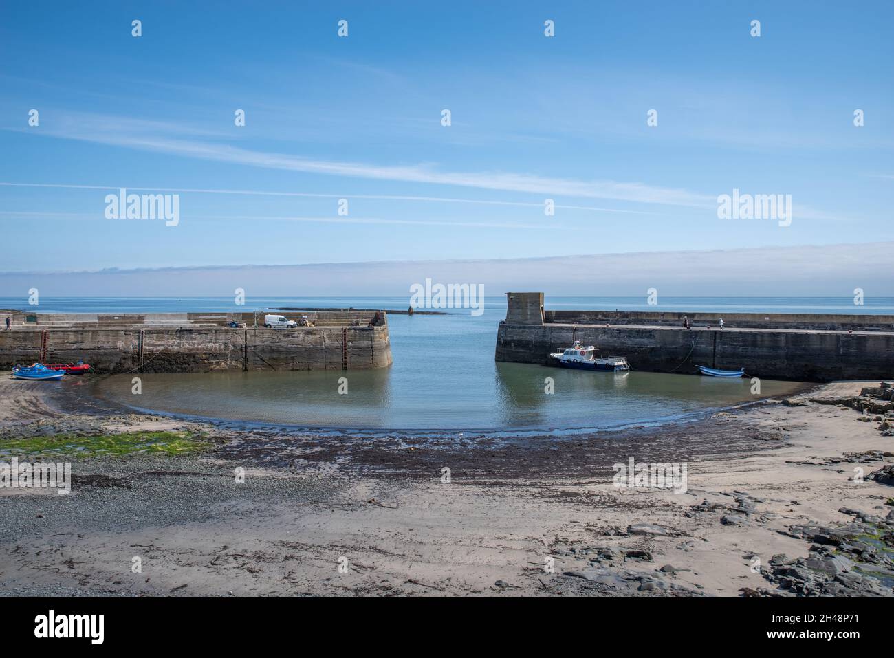 Craster, Northumberland, England, 23rd July, 2021 - Craster walled harbour at low tide with small boats and blue sky background. Stock Photo
