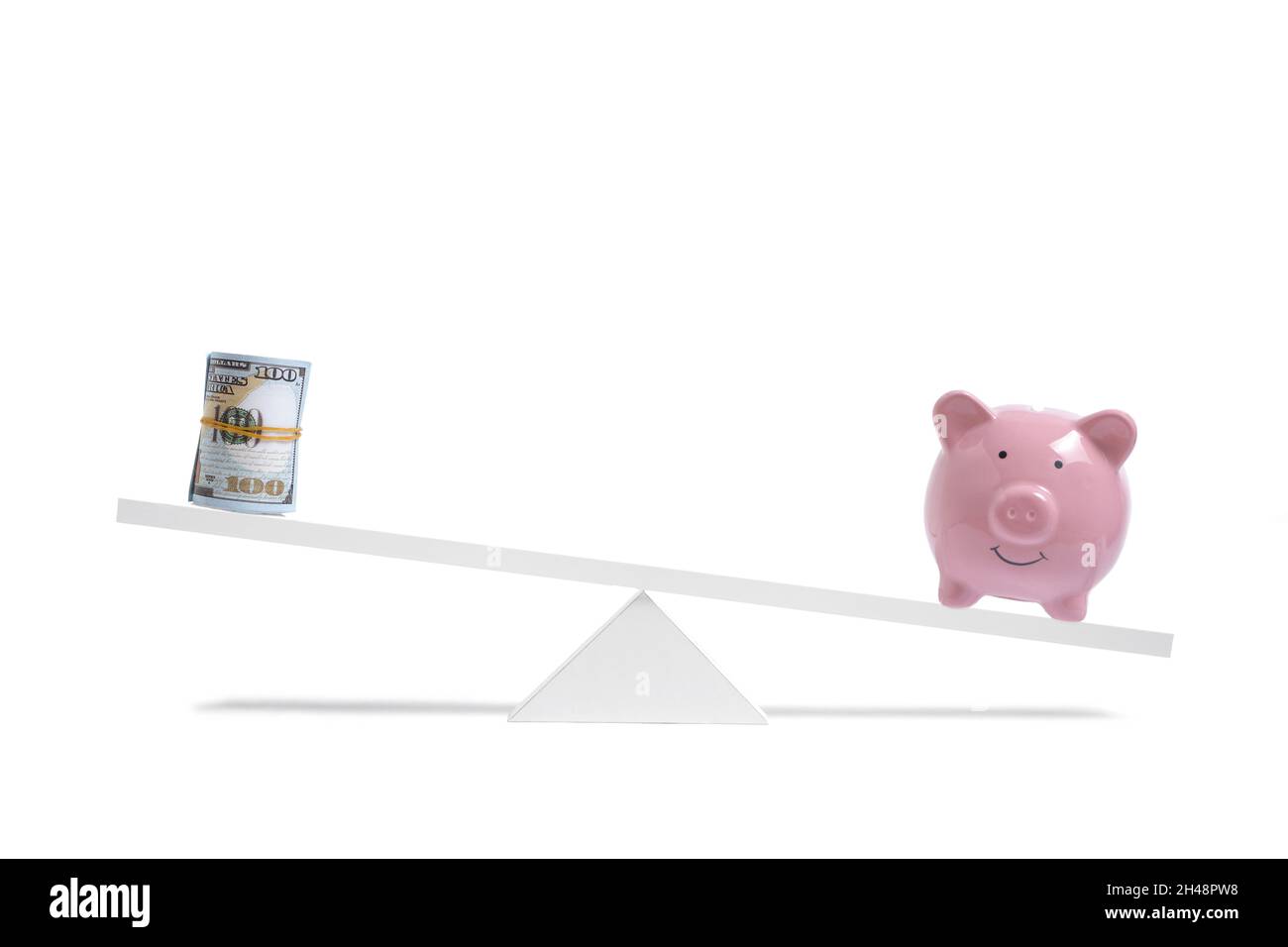 Piggy bank on scales outweighs roll of hundred dollar bills, on white background, business and savings Stock Photo