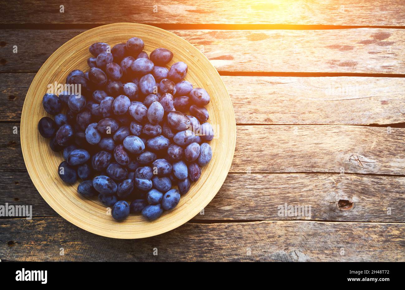 Plate with plums on a rustic wooden background, top view Stock Photo