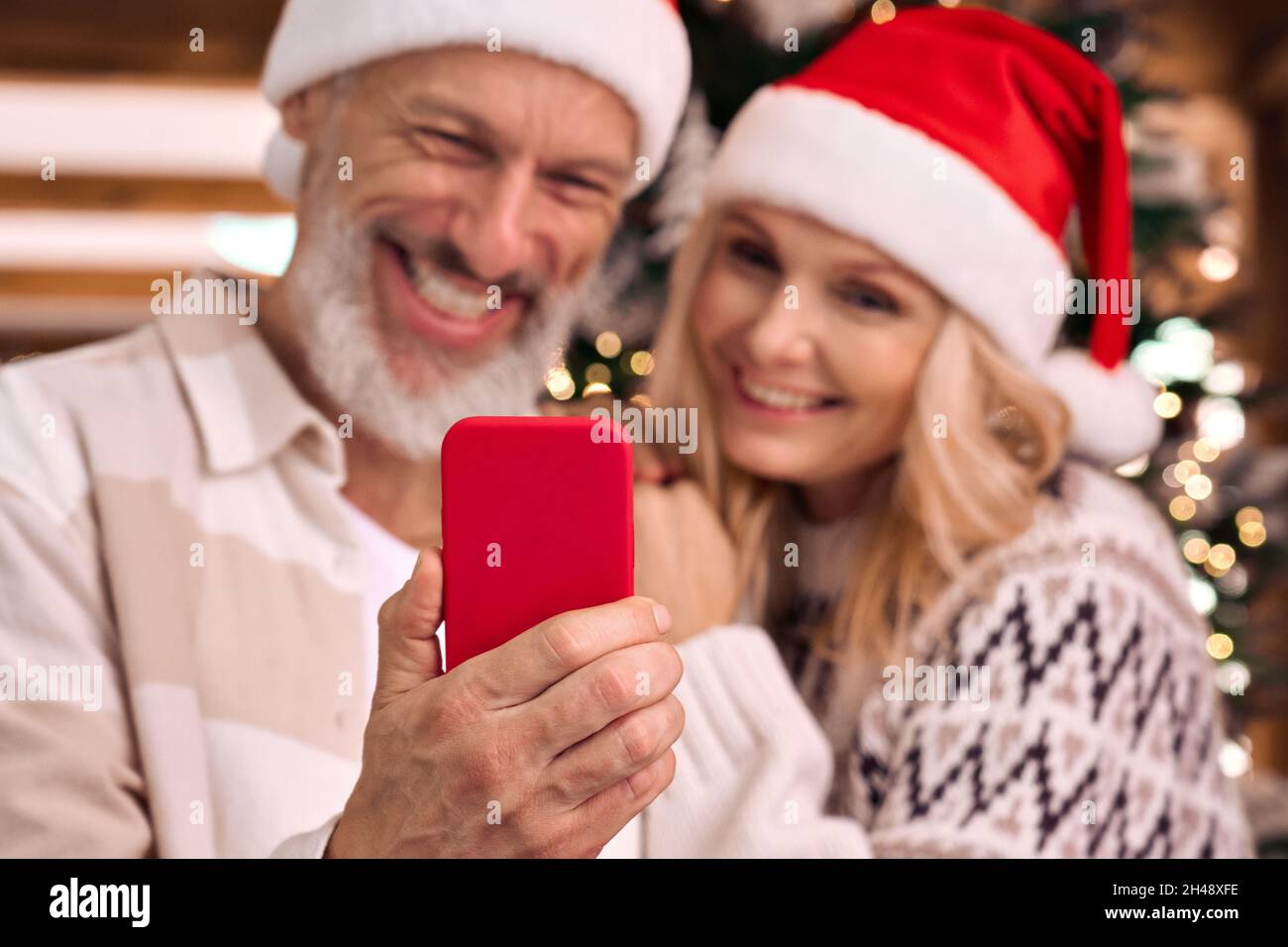 Happy mature family couple in santa hats using cell phone on Christmas. Stock Photo