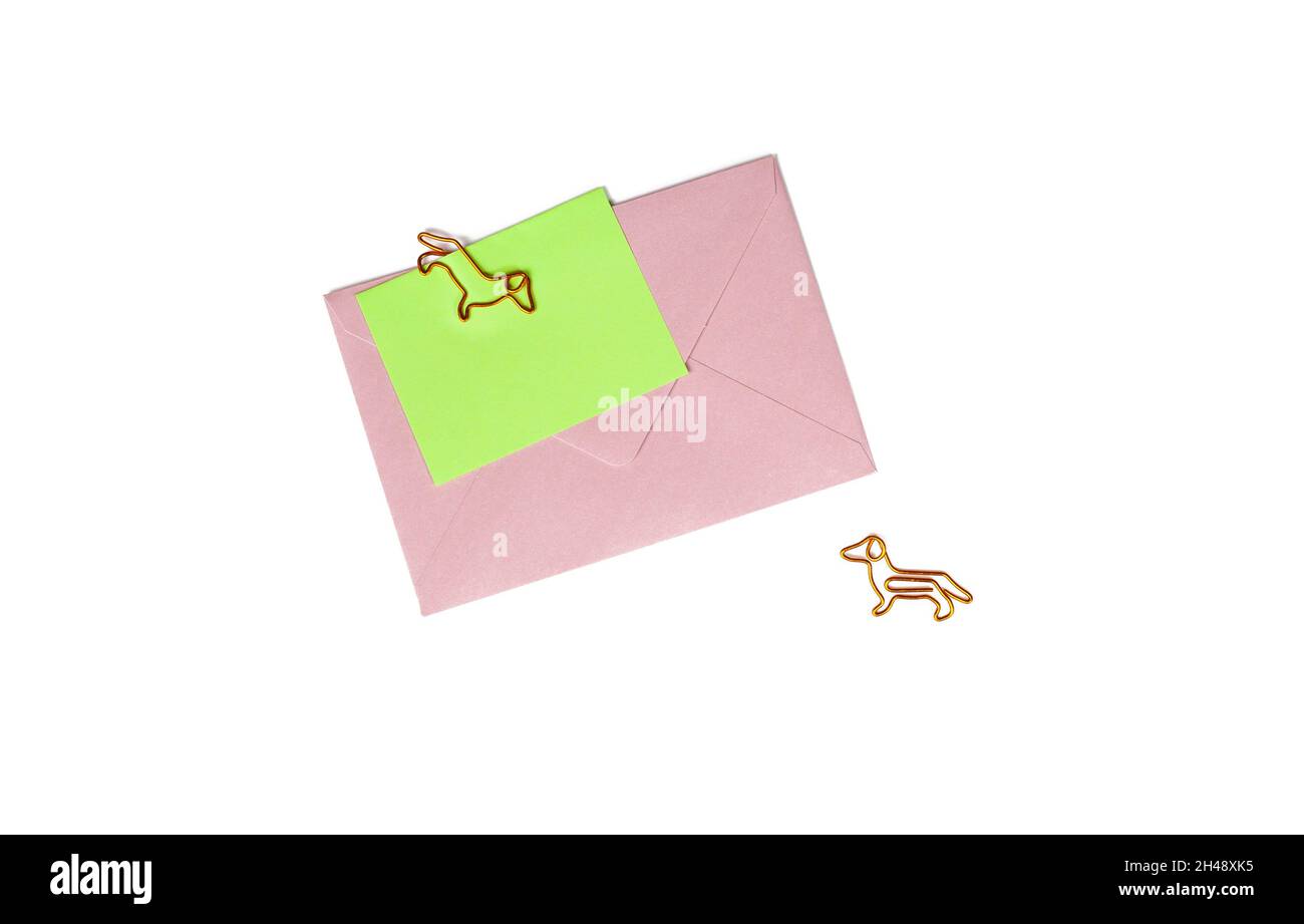 Pink paper envelope with blank note and dog-shaped paper clip on white background. Office supplies for a good mood. reminder on paper. Close up Stock Photo