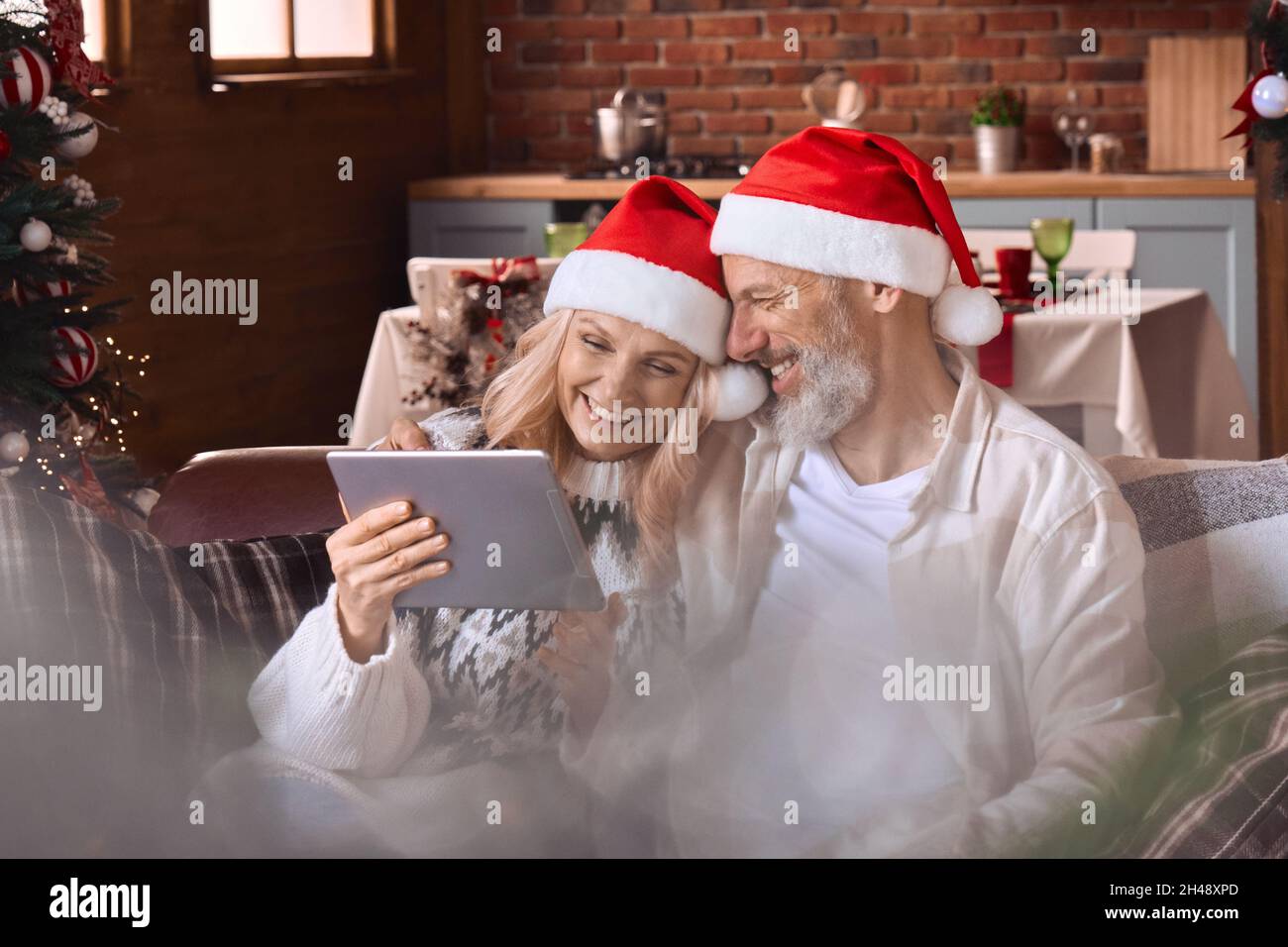 Happy old couple using digital tablet feeling joy have virtual Christmas party. Stock Photo
