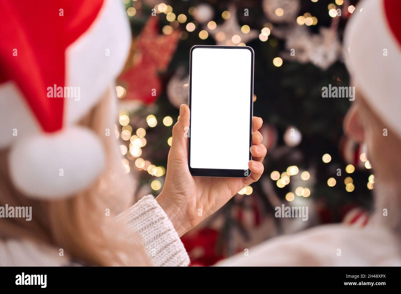 Happy family couple in santa hats using cell phone mockup screen on Christmas. Stock Photo