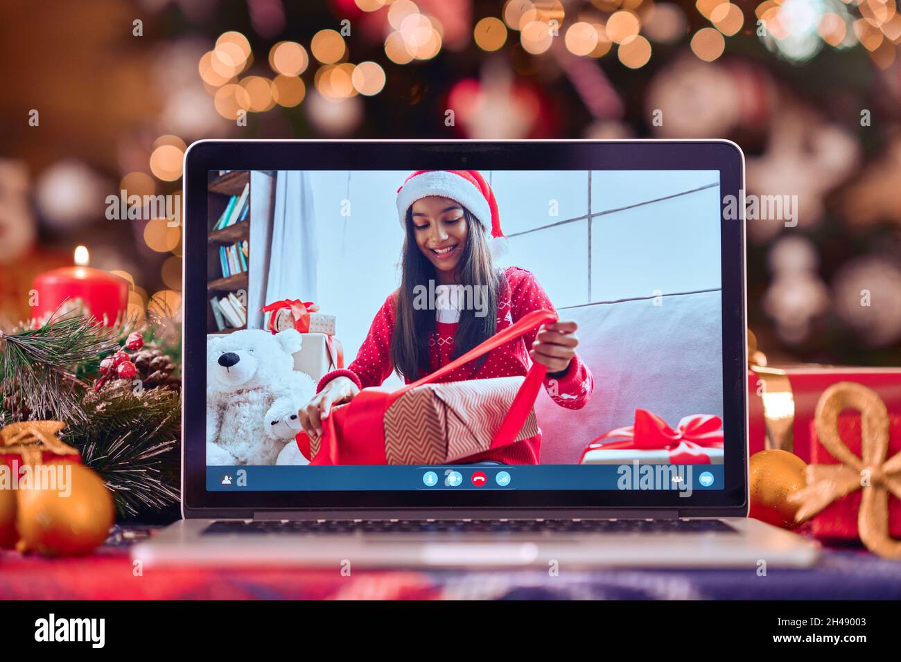 Teen girl opens gift on video call laptop screen on Christmas table background. Stock Photo