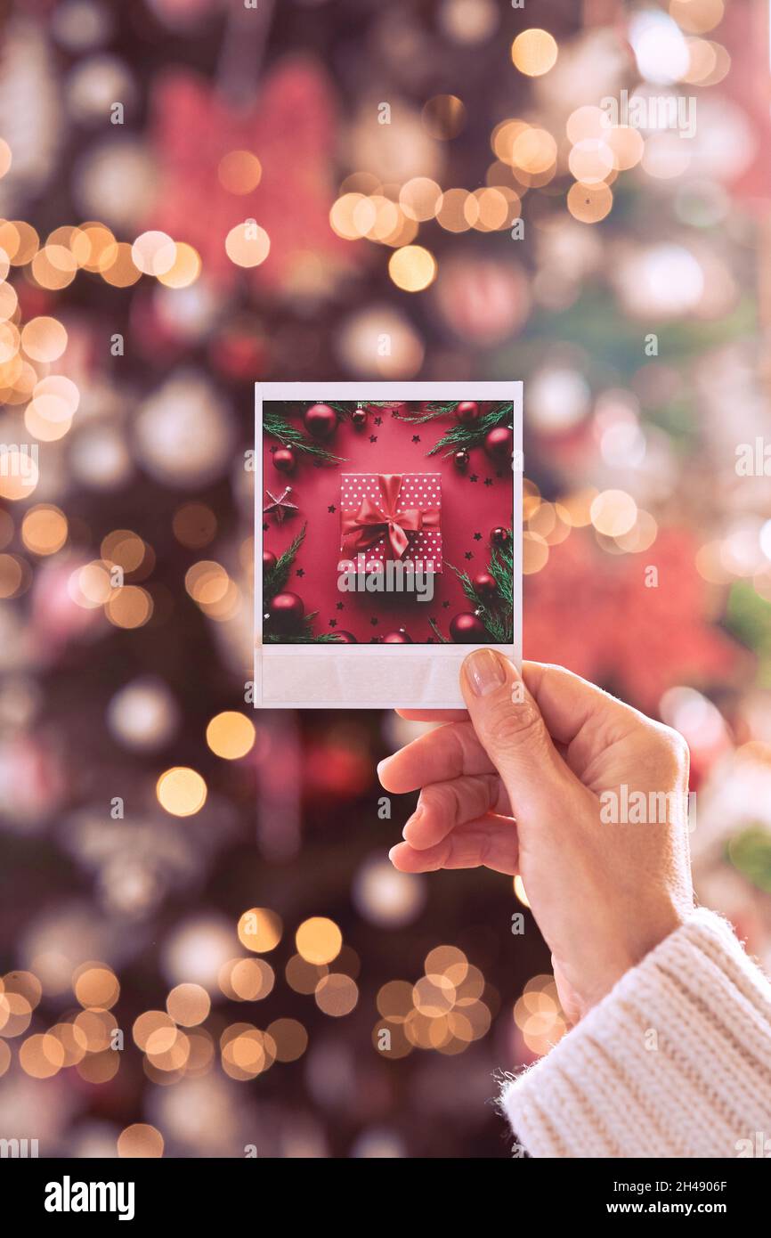 Female hand holding Christmas card with gift on xmas tree background. Stock Photo