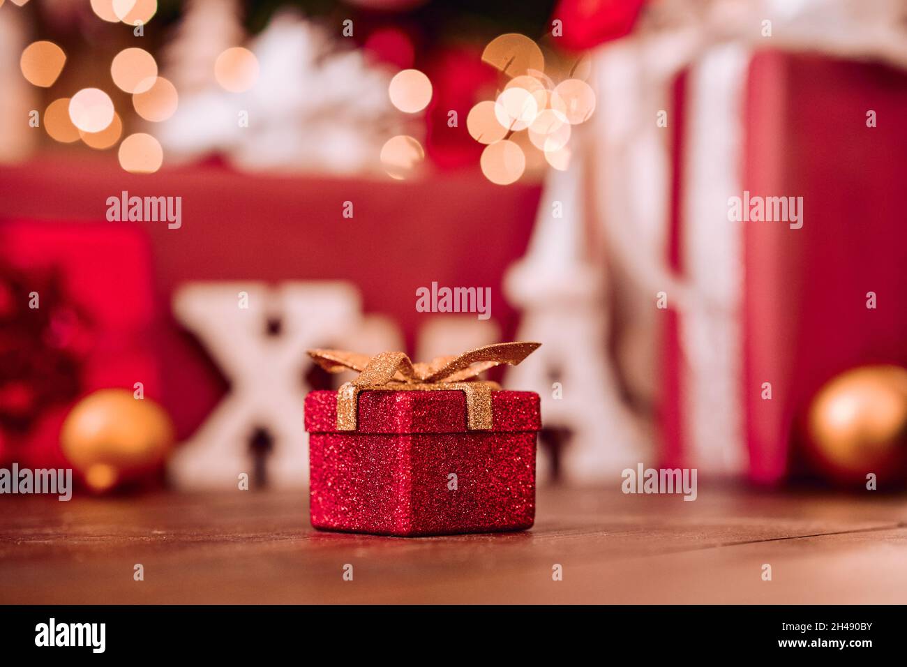 Small red Xmas present gift box under Christmas tree background. Stock Photo