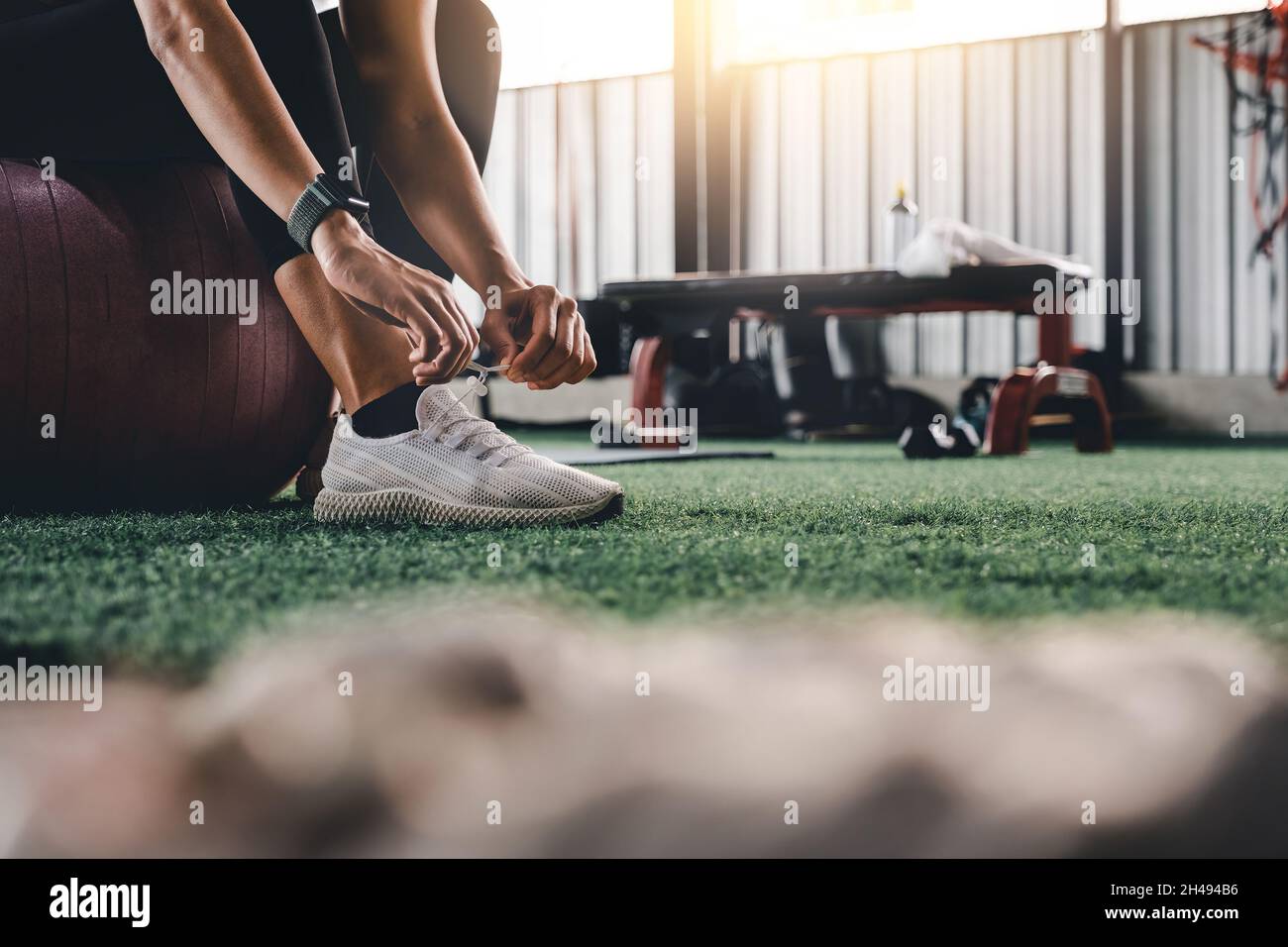 Woman sitting on gym ball tying shoelace and getting ready for fitness Stock Photo