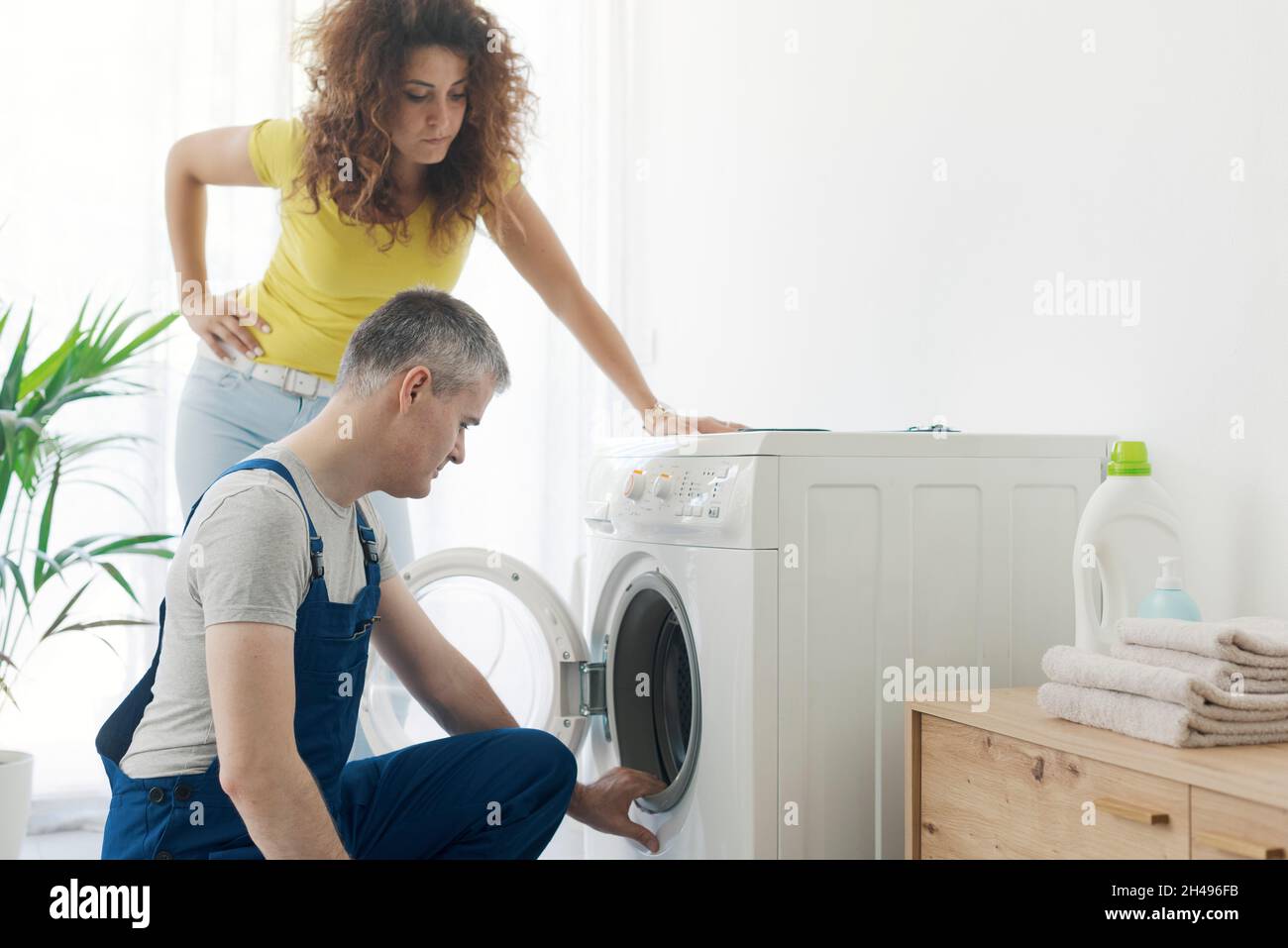 Repairman checking a broken washer, the customer is standing next to