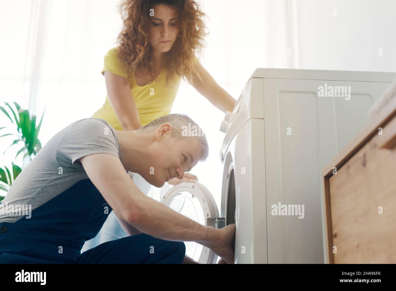 Repairman checking a broken washer, the customer is standing next to