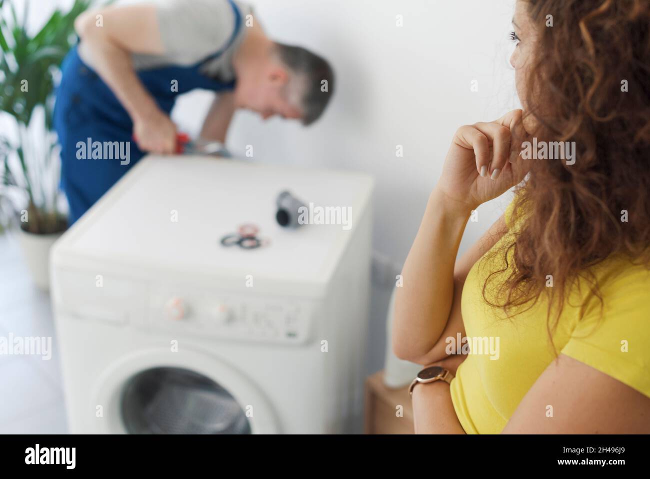 Professional plumber repairing a broken washing machine, the customer is looking at him, repair service concept Stock Photo