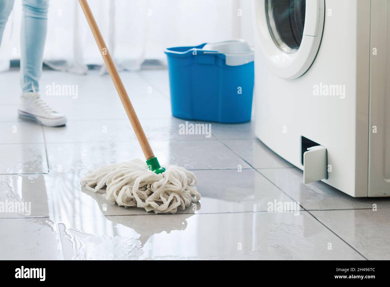 Broken washing machine leaking on the floor, a woman is cleaning with a