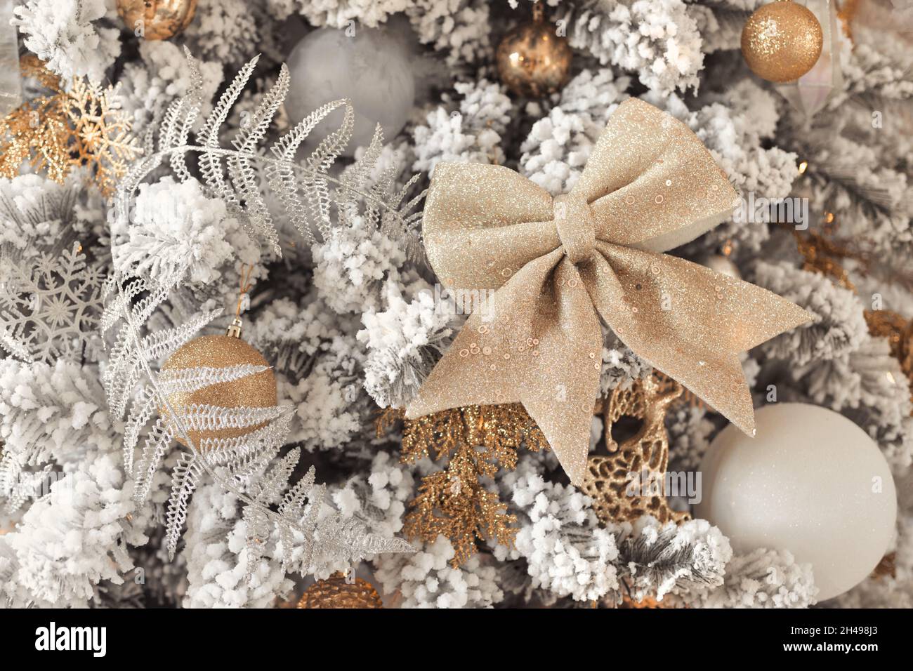 Close up photo of toy balls in silver and gold on luxury snowy Christmas tree with big golden bow Stock Photo