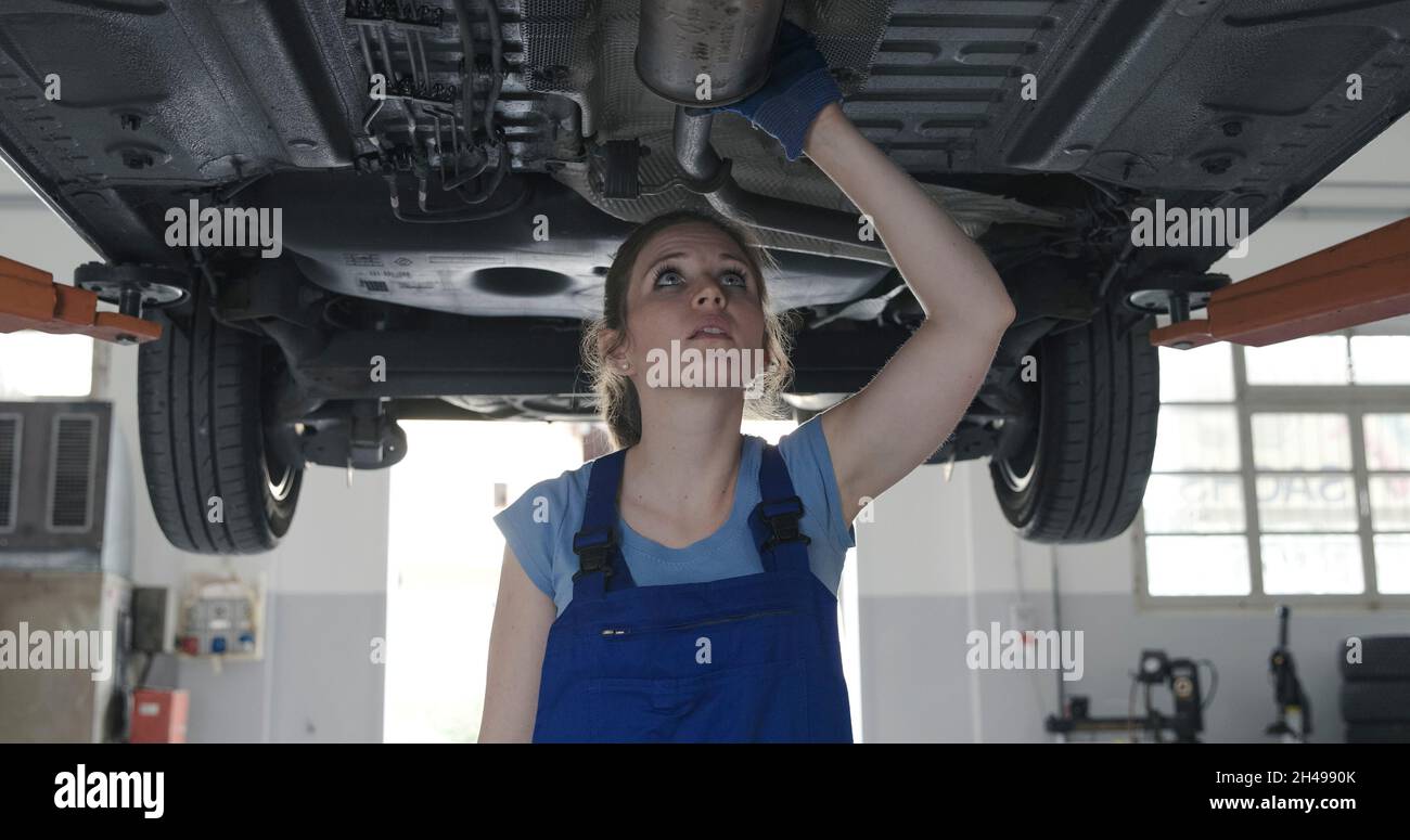 Female mechanic working under a car in the auto repair shop, she is