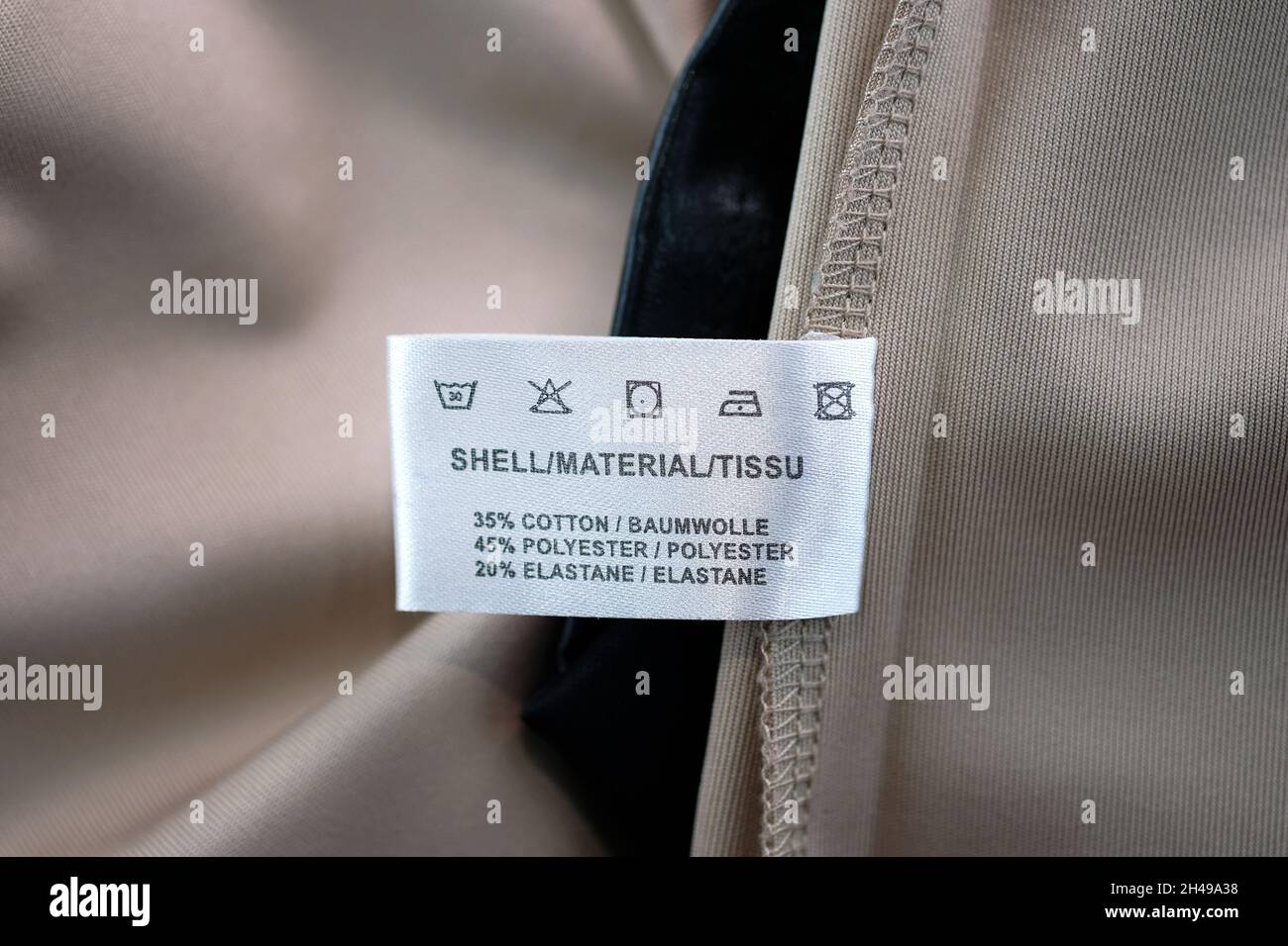 Garment label on the dress with washing care instructions. Label for wash close up. Beige polyester, cotton and elastane clothing. Stock Photo