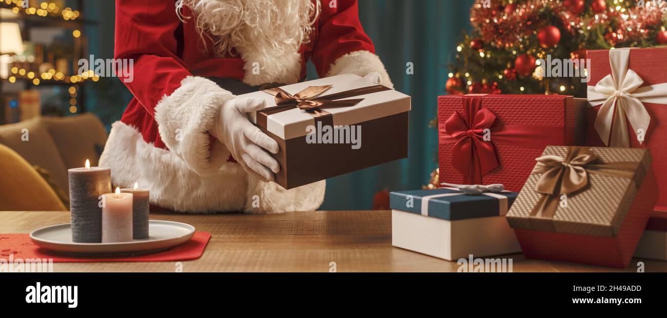 Santa Claus putting Christmas gifts on a table, holiday and celebration