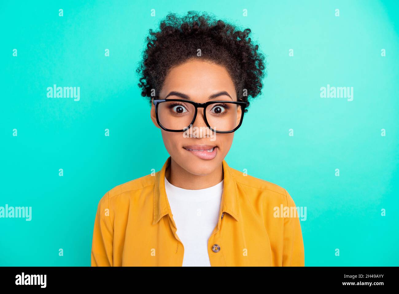 Photo portrait girl curly hairstyle wearing glasses biting lip isolated vivid teal color background Stock Photo