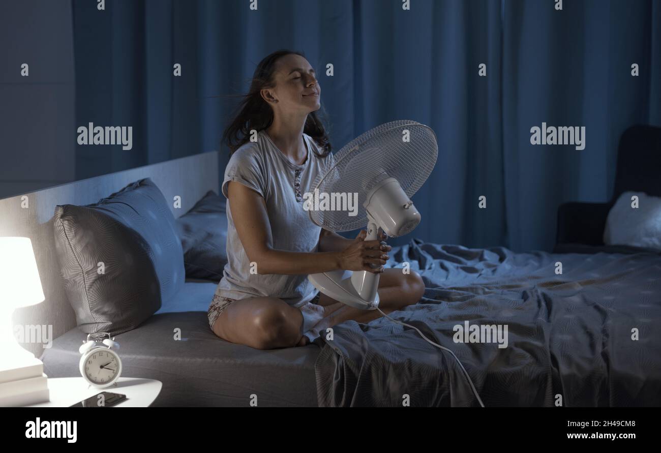 Woman in her bedroom on a hot summer night, she is enjoying fresh air in front of a fan Stock Photo
