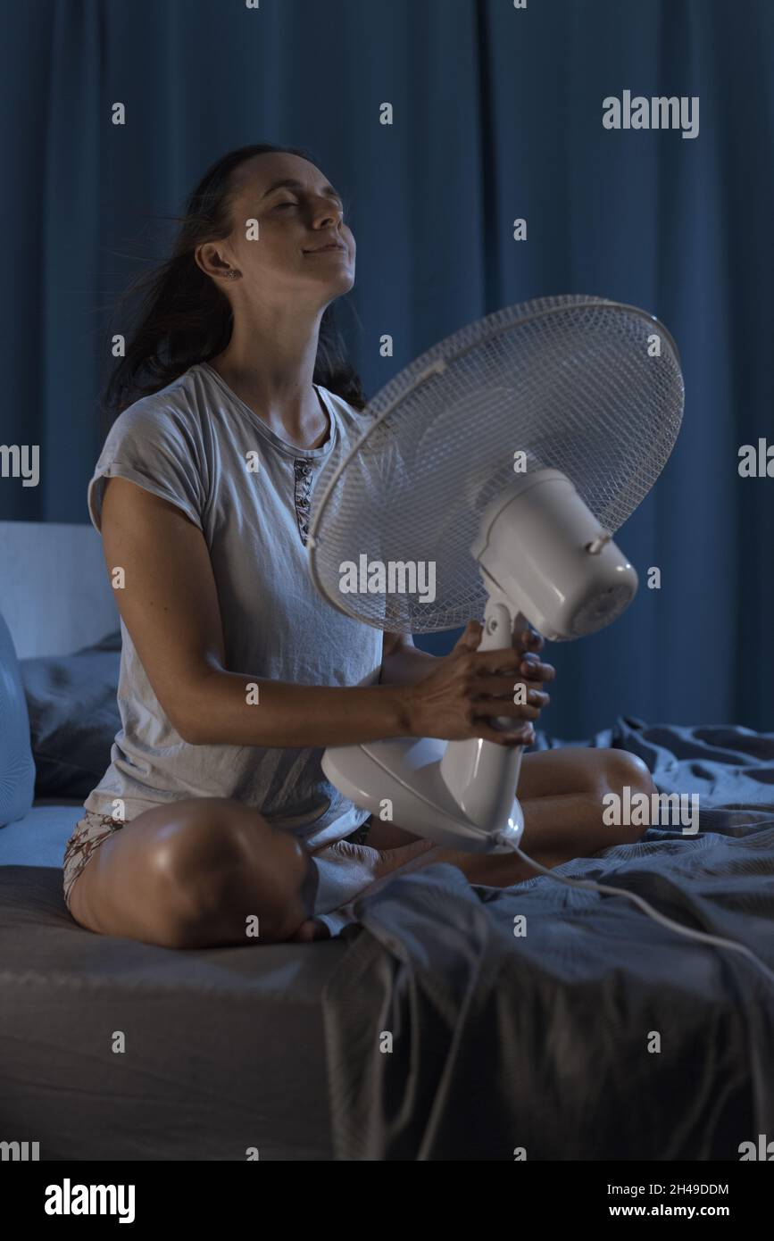 Woman in her bedroom on a hot summer night, she is enjoying fresh air in front of a fan Stock Photo