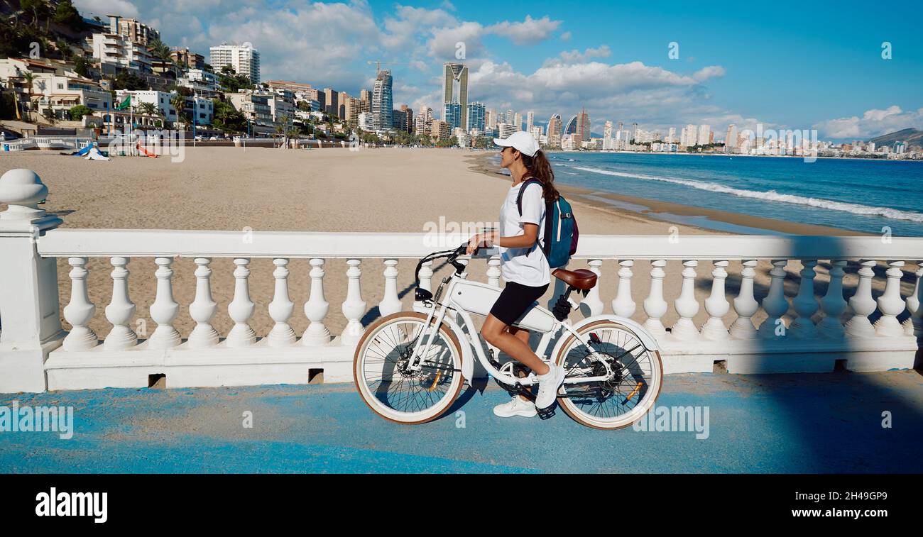 Happy woman tourist with electric bicycle over background Levante beach overlooking panorama of Benidorm city. traveler concept Stock Photo
