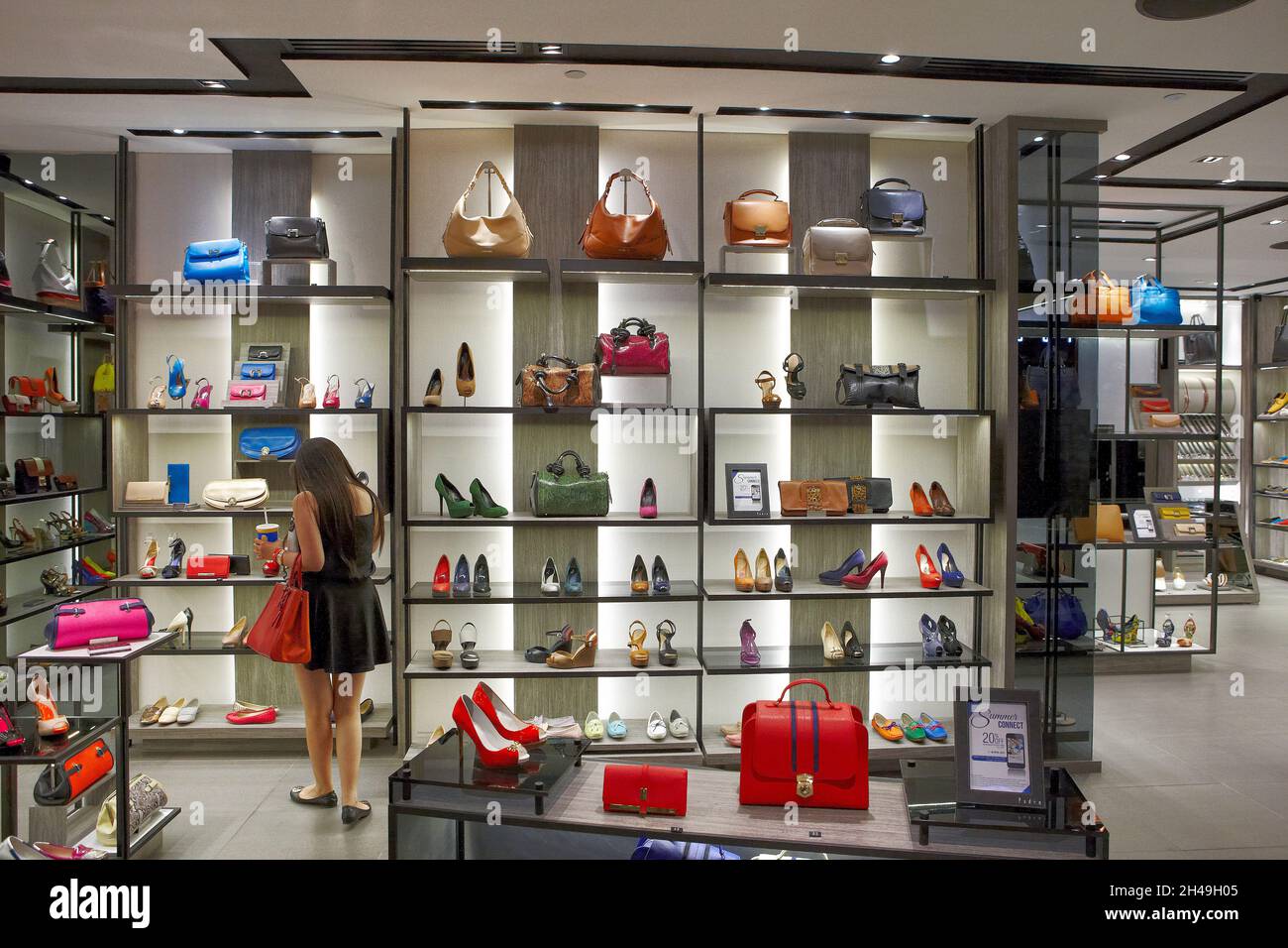 Young Asian woman looks at selection of luxury leather bags and shoes displayed in the ION Orchard Shopping Centre. Orchard Road, Singapore. Stock Photo