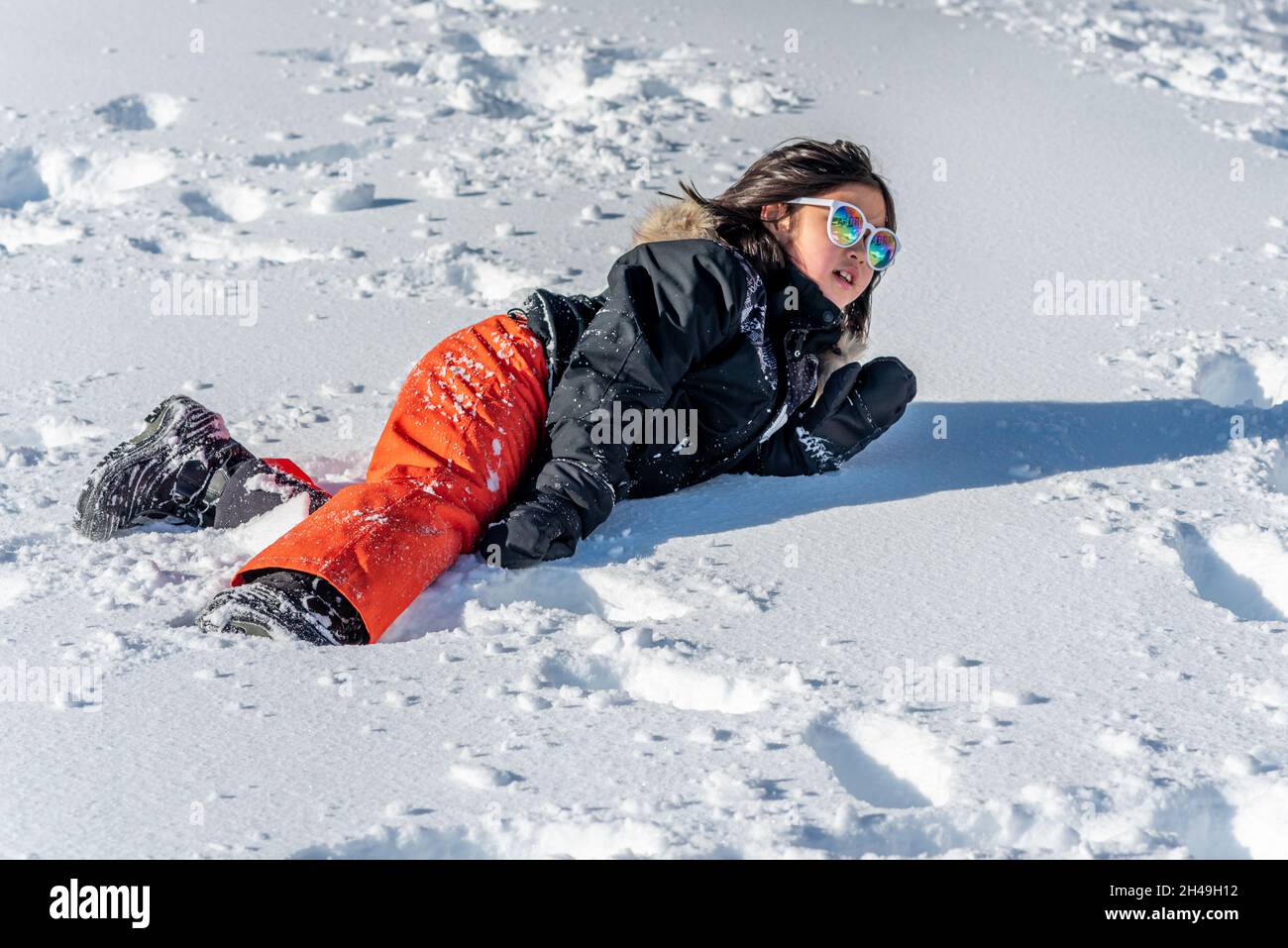 Child falling down in snow. One Asian girl lying on the ground in winter. Sliding danger. Stock Photo