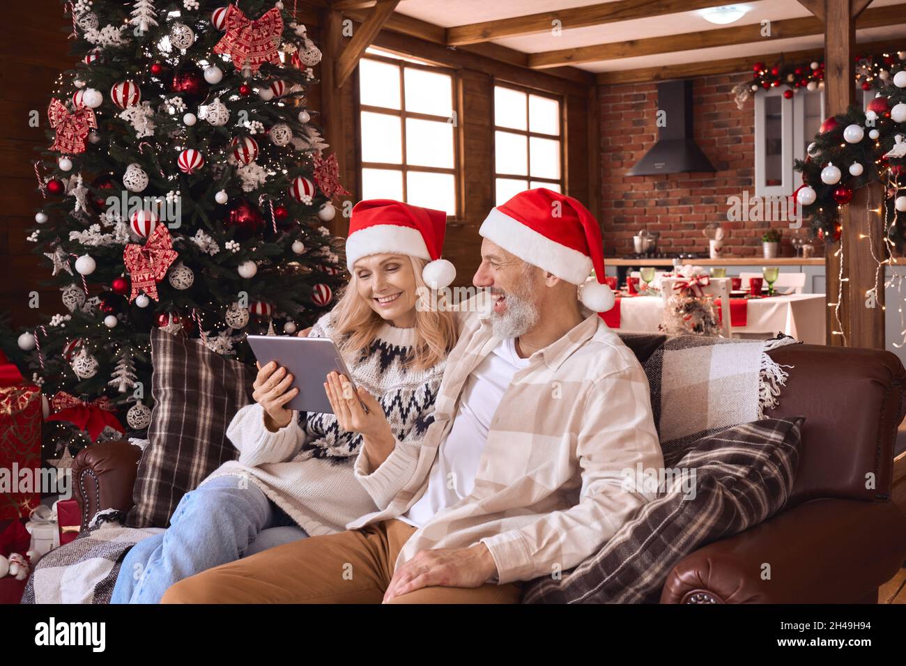 Happy 50s older couple using digital tablet in living room on Christmas. Stock Photo