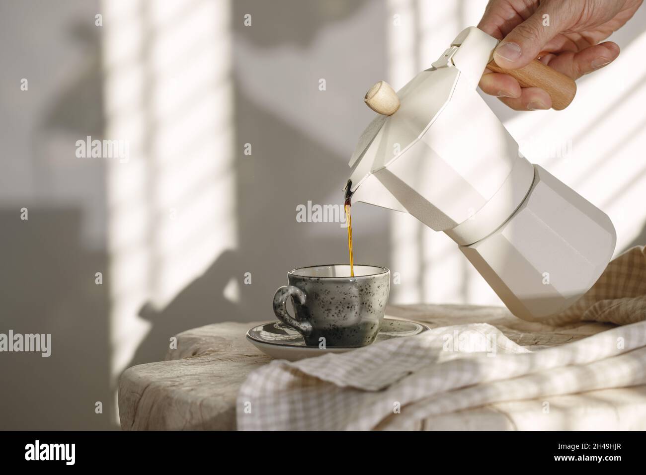 https://c8.alamy.com/comp/2H49HJR/pouring-coffee-from-italian-coffee-maker-with-wooden-handle-into-grey-espresso-craft-cup-on-solid-wood-stump-decorated-with-linen-tea-towel-in-creamy-2H49HJR.jpg