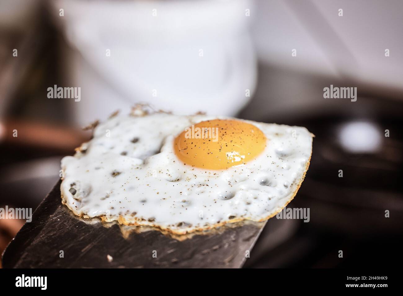 Single fried egg sprinkled with ground black pepper resting on metal spatula Stock Photo