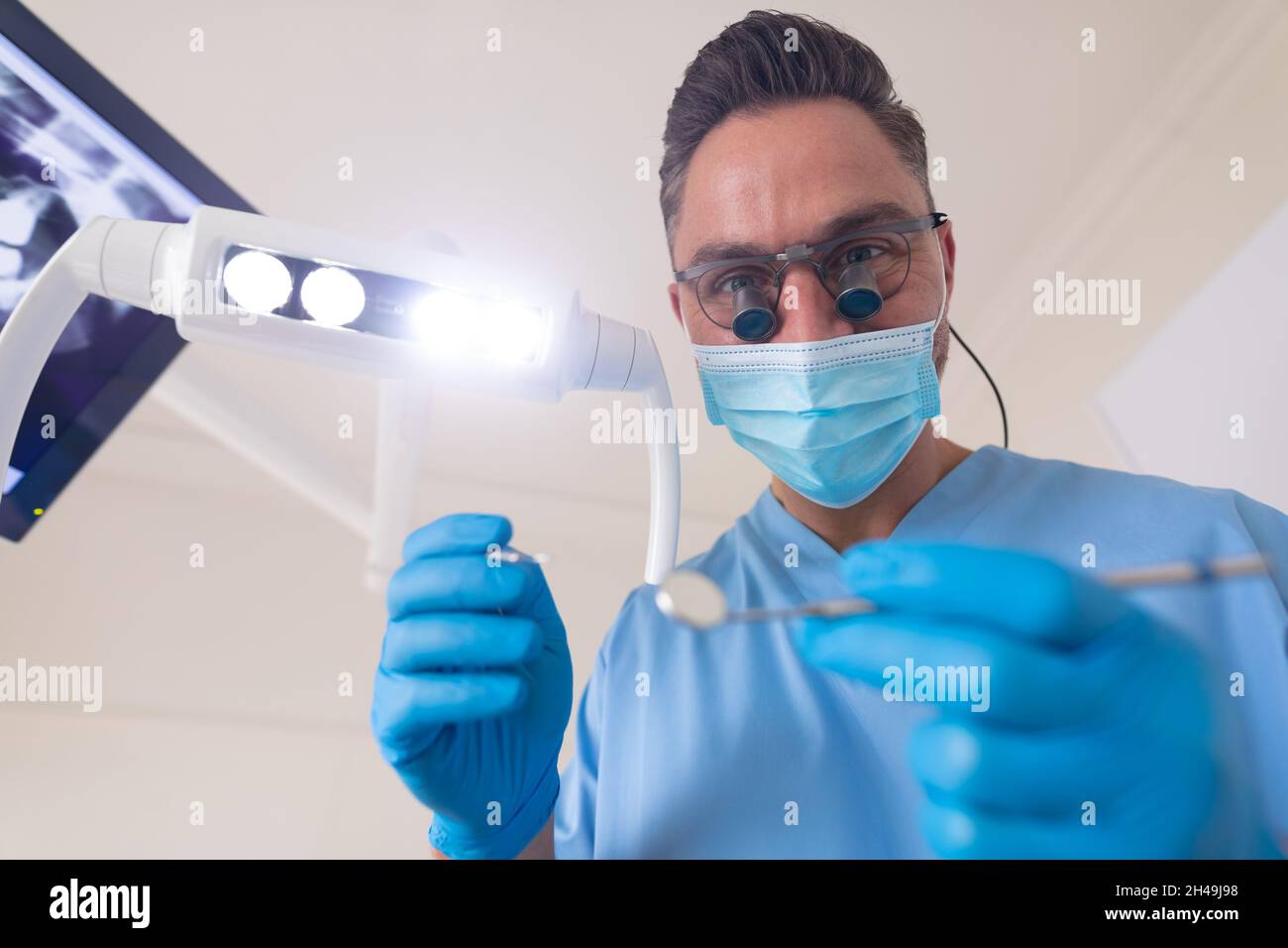 Caucasian male dentist wearing face mask holding dental tools at modern dental clinic Stock Photo
