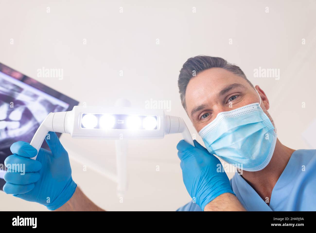 Caucasian male dentist wearing face mask holding lamp at modern dental clinic Stock Photo