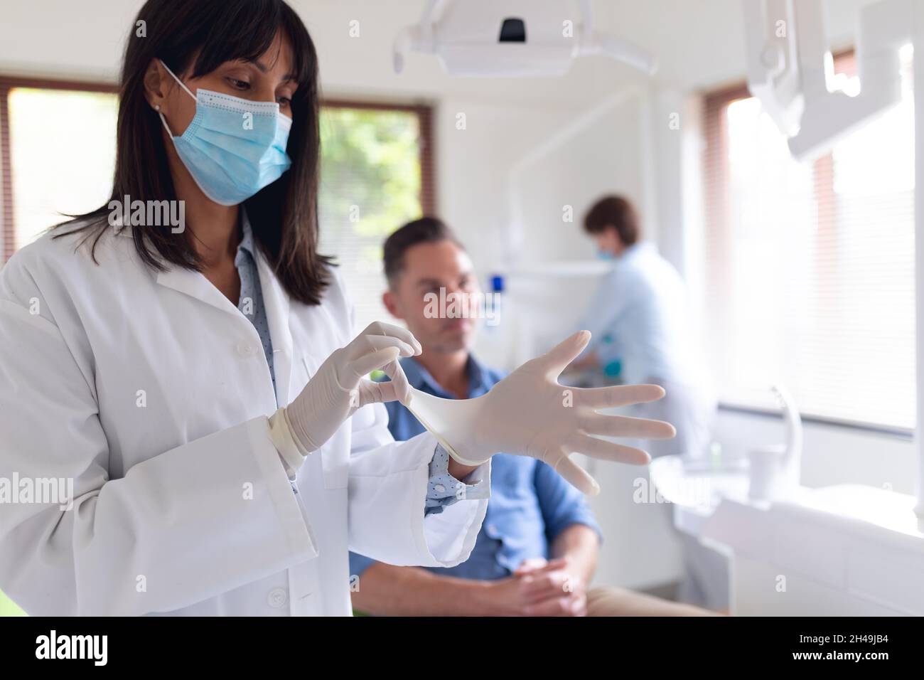 Biracial female dentist wearing medical gloves and male patient waiting at modern dental clinic