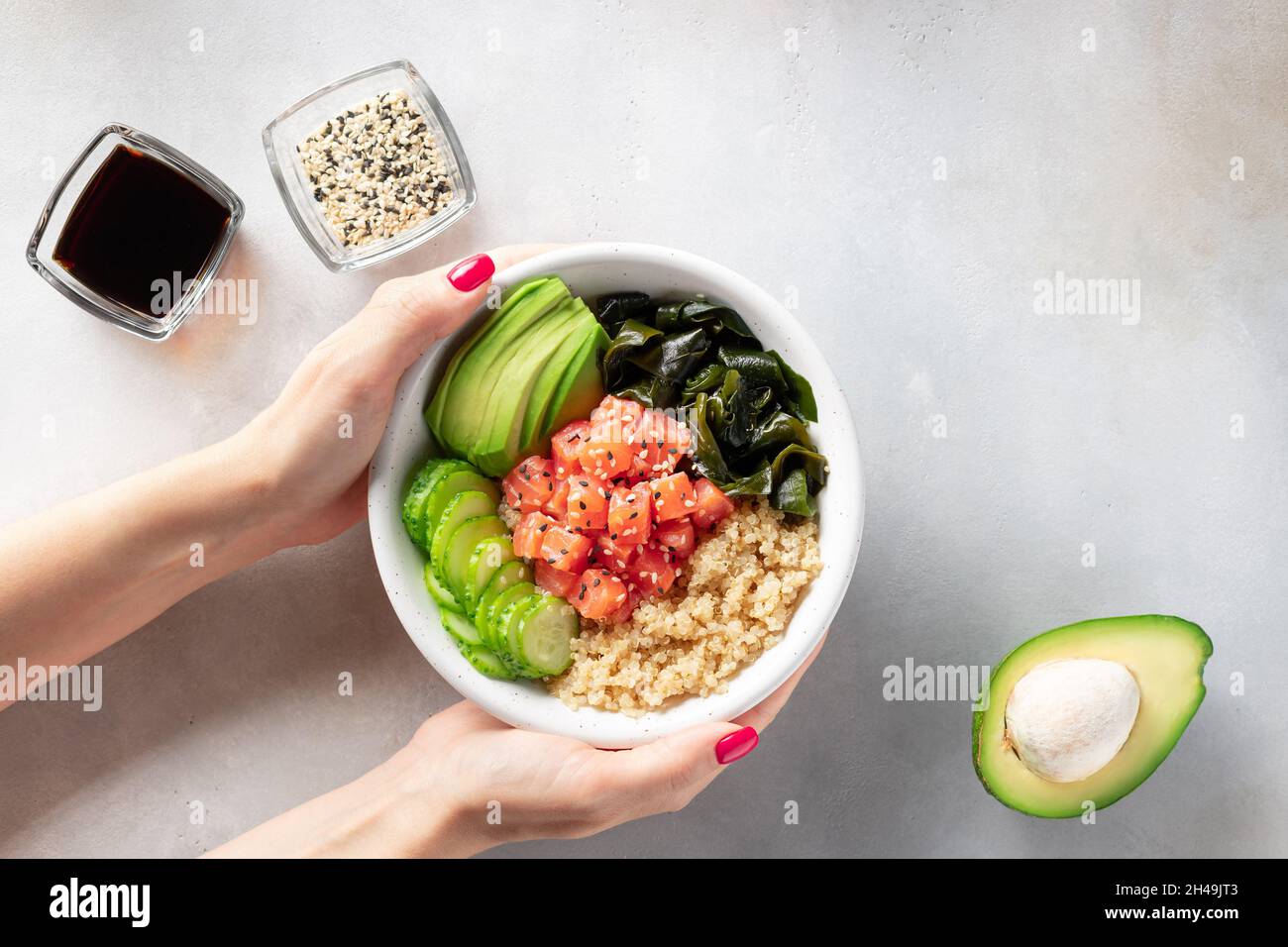 female hand holding bowl with quinoa, salmon, avocado, wakame seaweed