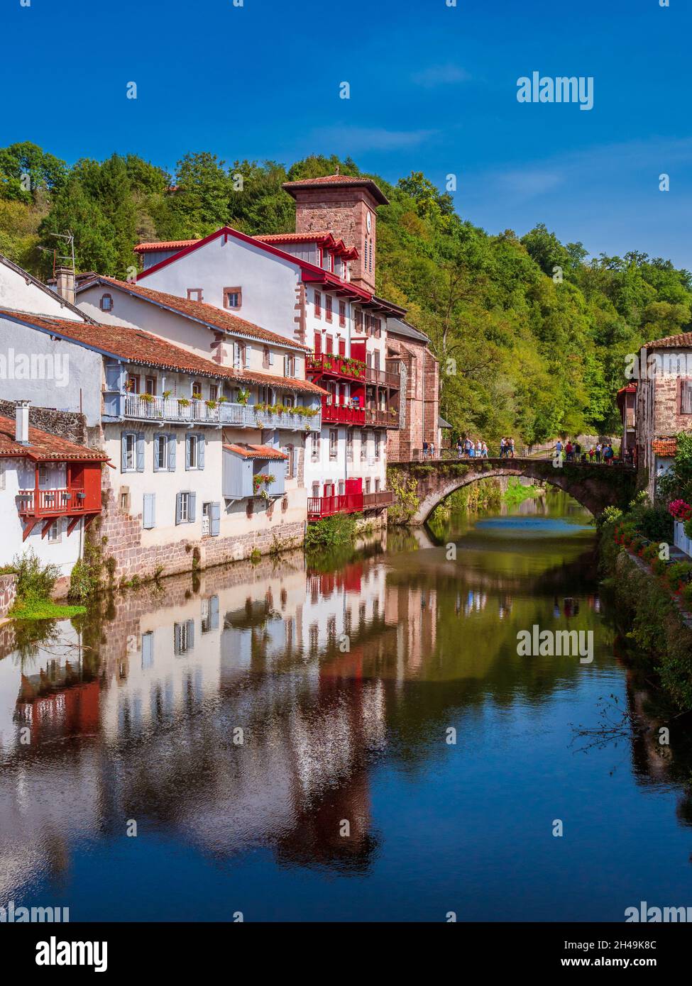 Panoramic view of French white town with red balconies and flowers crossed by a tranquil river. Saint-Jean-Pied-de-Port, France Stock Photo